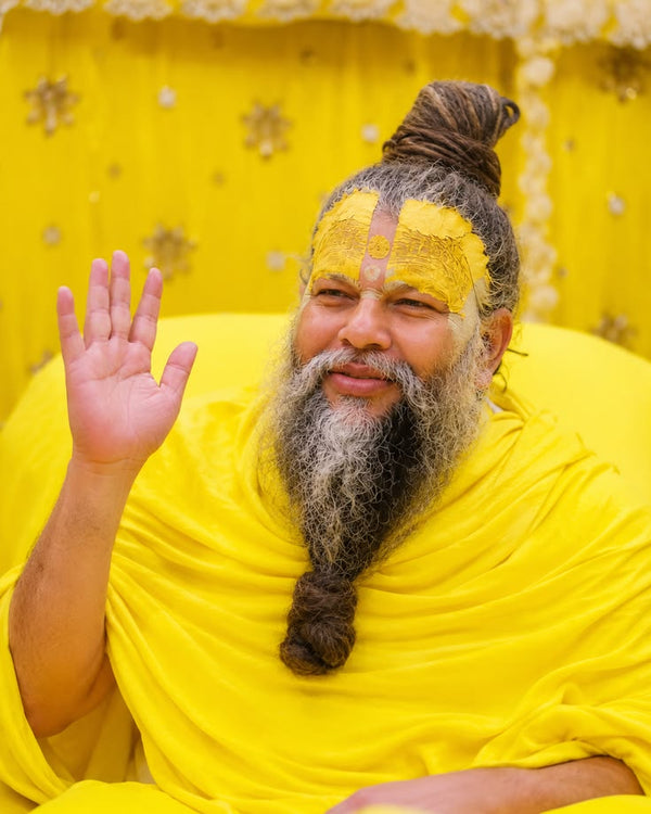 Spiritual teacher in yellow robes with traditional yellow face paint, raising his hand