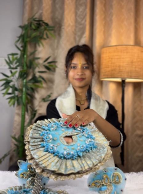 Woman presenting a blue and silver Laddu Gopal poshak with matching accessories